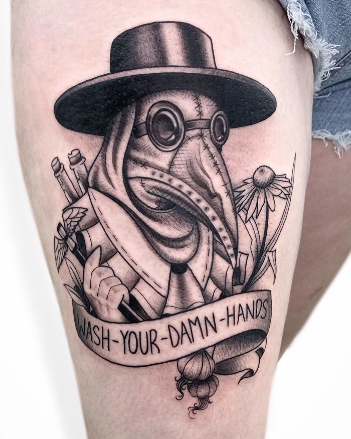 Plague doctor Covid-19 tattoo with flowers and "Wash Your D**n Hands" banner.