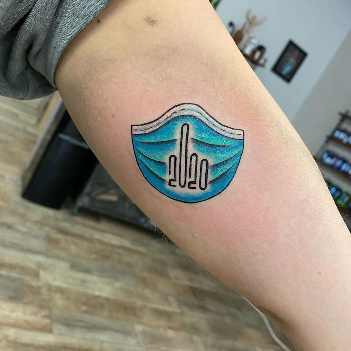 Creative Covid-19 tattoo featuring a blue surgical mask with 2020 design, inked on an arm in a tattoo studio.