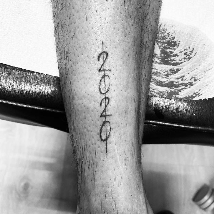 Black tattoo of "2020" on a person's forearm, symbolizing a Covid-19 theme, in a creative vertical design.