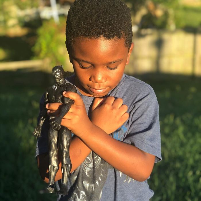Young boy holding Black Panther action figure in a heartfelt memorial honoring the late Black Panther character outdoors.
