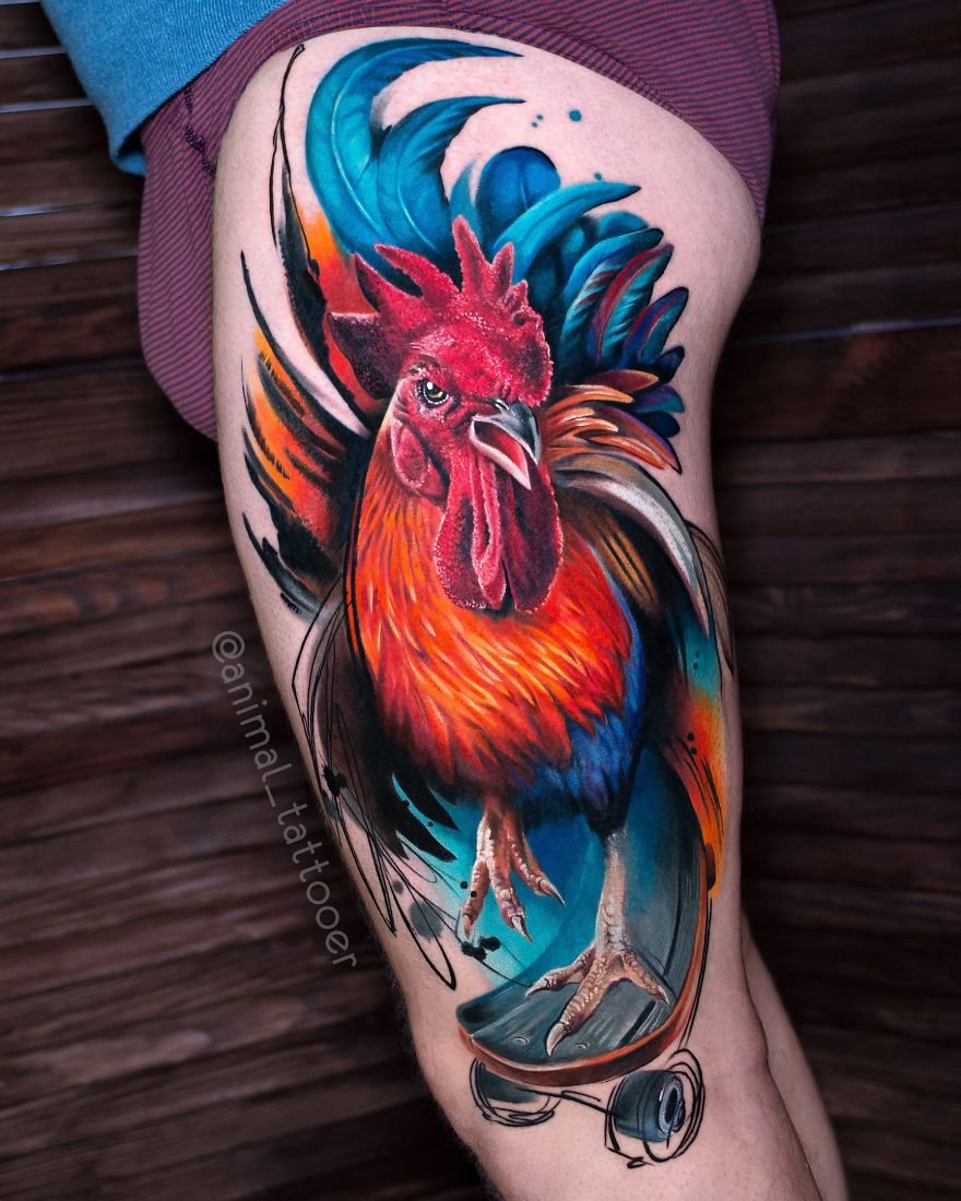 Colorful and bright animal tattoo of a rooster on a person's thigh, featuring vibrant blue and orange hues.