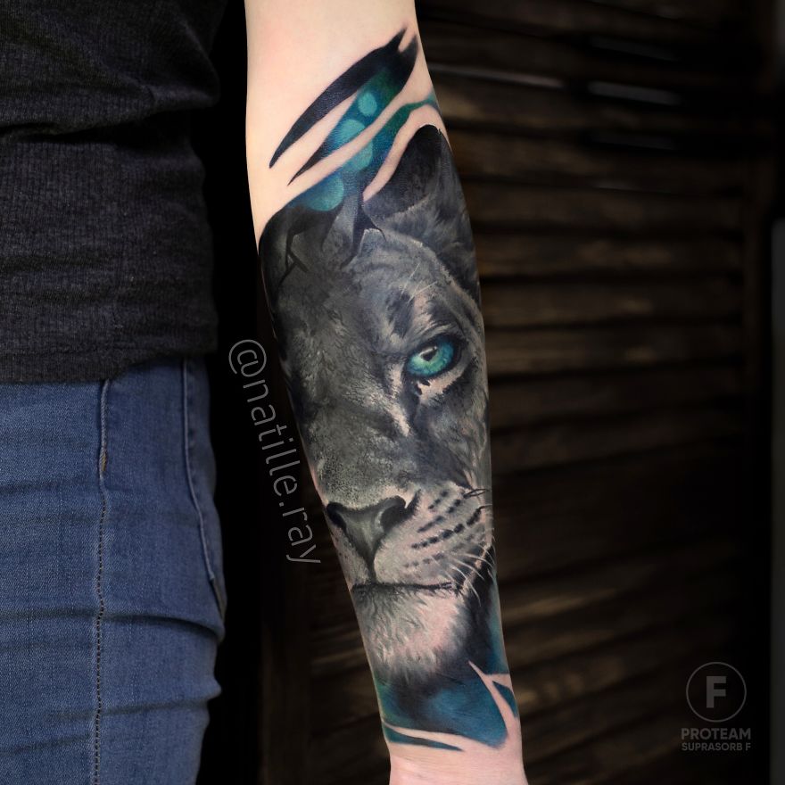 Colorful animal tattoo of a lion on forearm, featuring vibrant blue and gray tones.