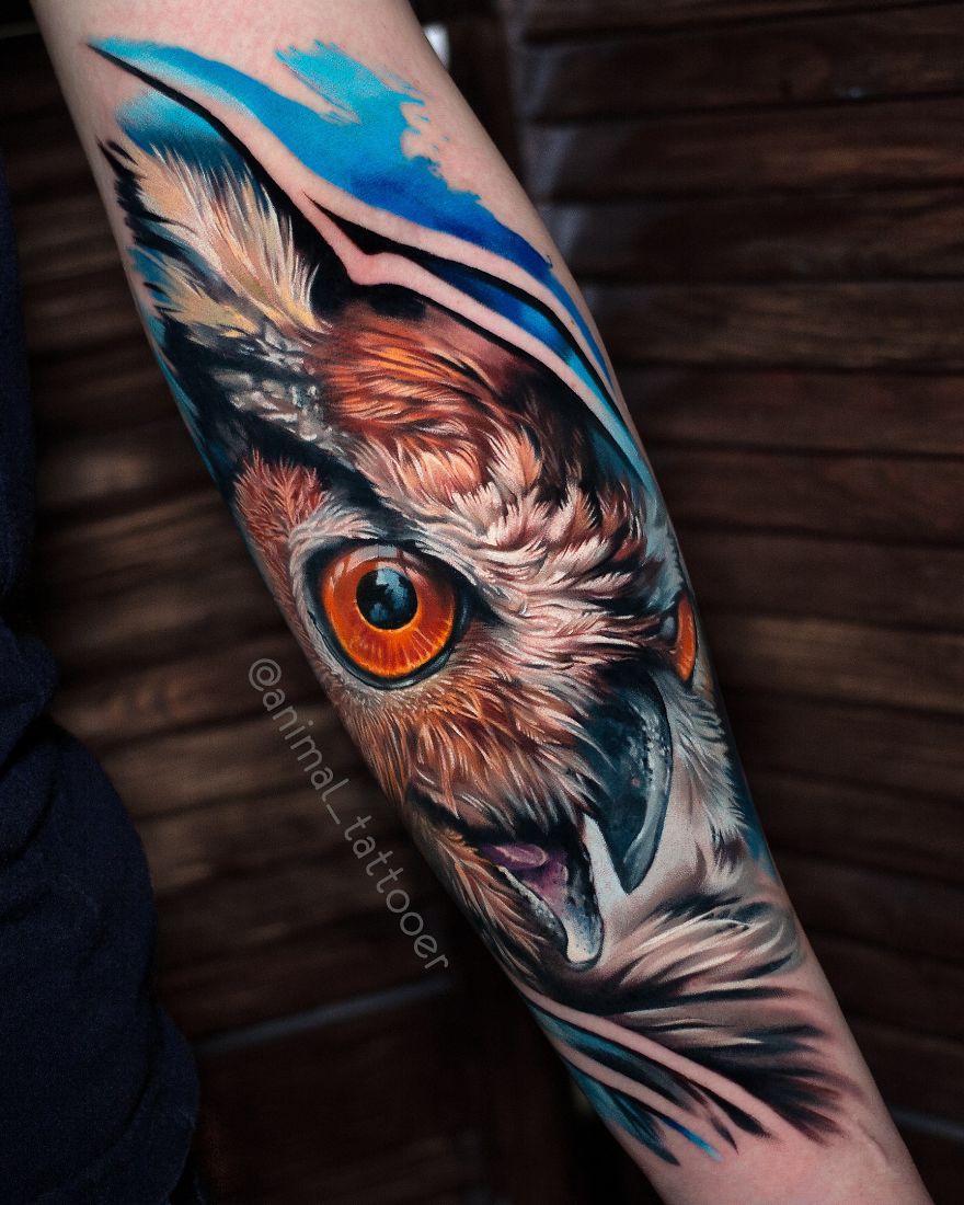Colorful and bright animal tattoo of an owl with vivid orange eyes and blue accents on forearm.