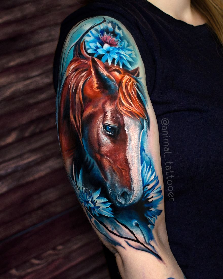 Colorful animal tattoo of a horse with blue flowers on a person's upper arm.
