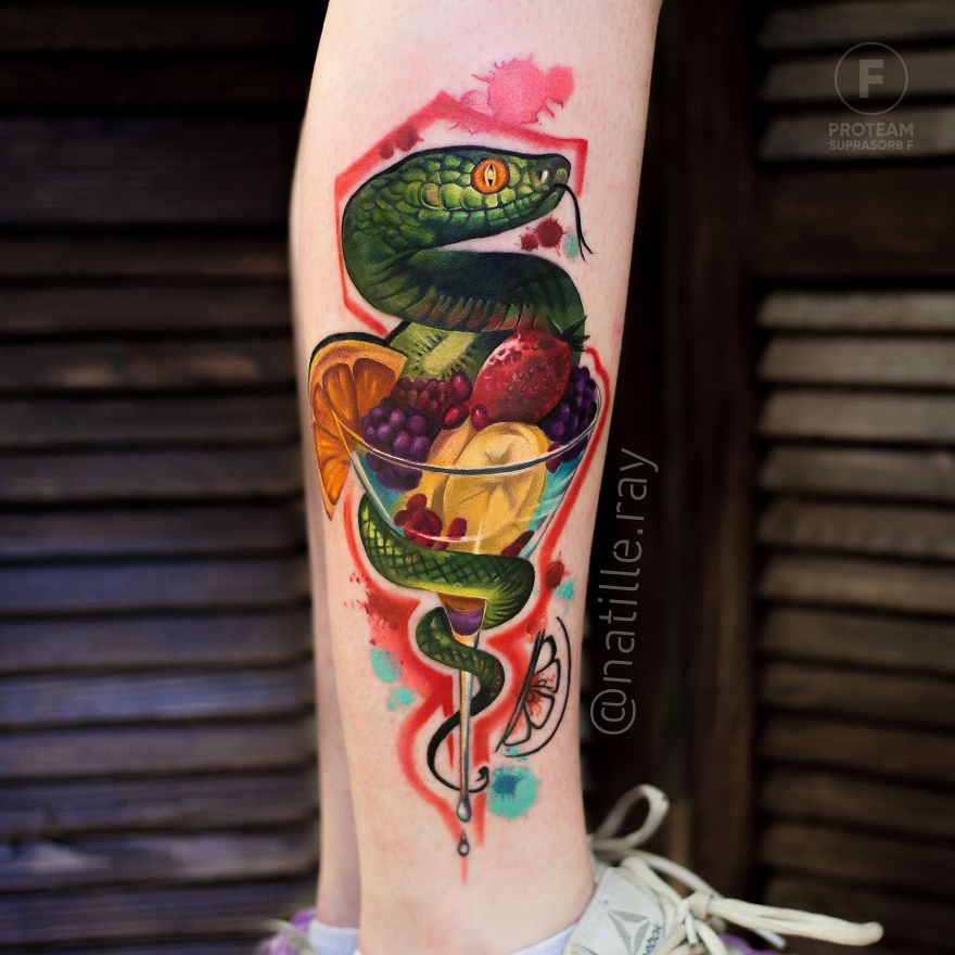 Colorful snake tattoo wrapped around fruits on a leg.