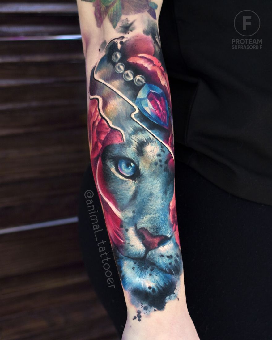 Colorful and bright animal tattoo of a big cat with vibrant blue eyes and red floral elements on a person's forearm.