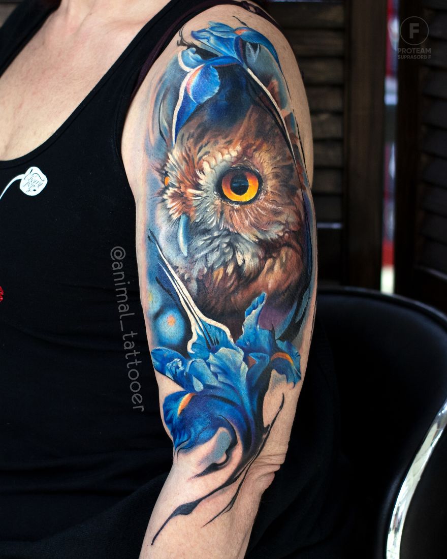 Colorful animal tattoo of an owl with blue flowers on a person's arm.