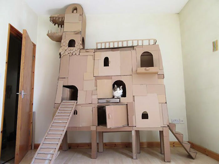 Cardboard fort for cats shaped like a castle, featuring ramps and multiple windows with a cat inside one opening.
