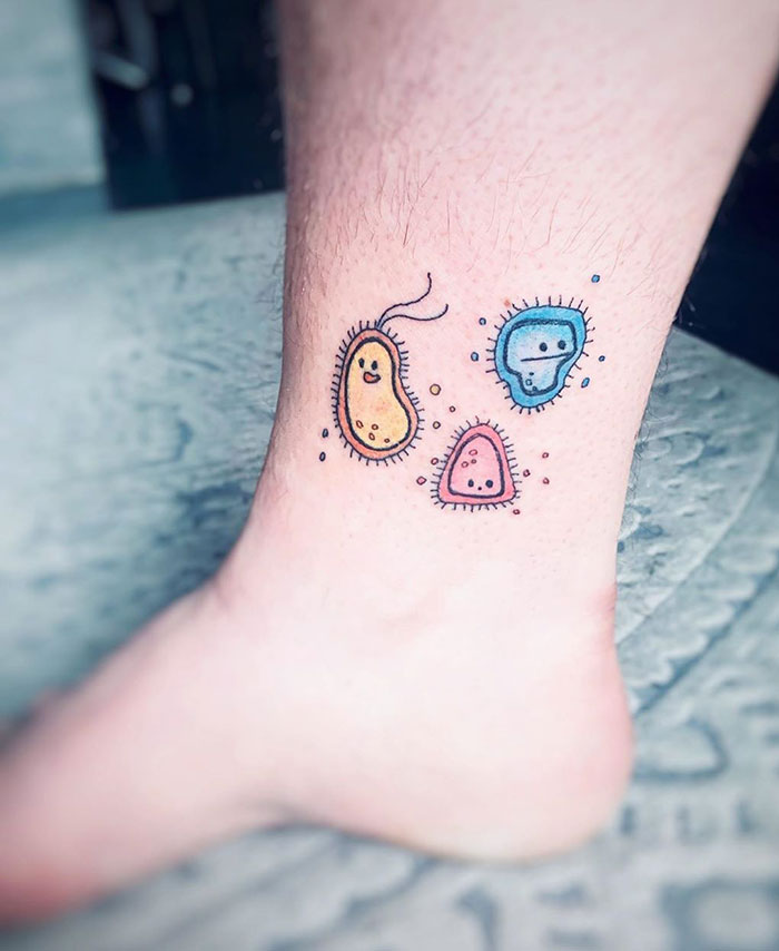 Colorful Covid-19 themed tattoo on a person's leg, featuring cute virus characters in blue, orange, and pink designs.
