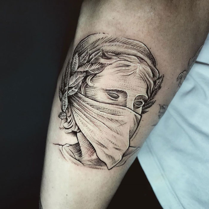 Tattoo depicting a classical bust wearing a mask, creatively representing Covid-19 themes with intricate shading.