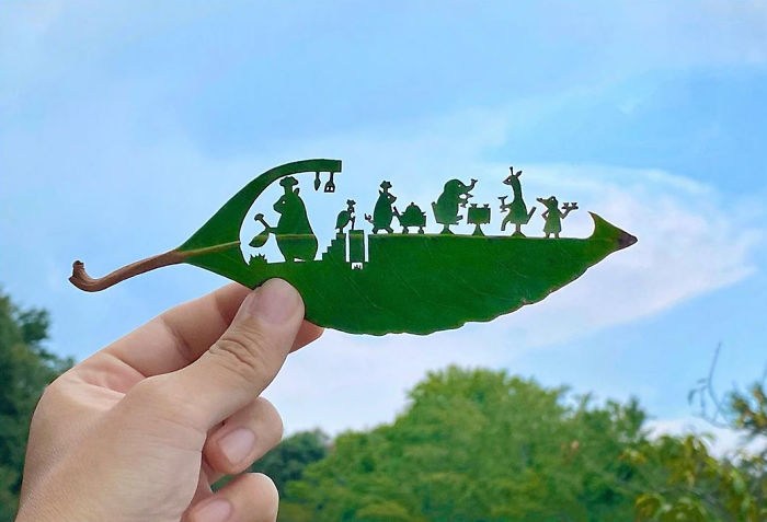 Hand holding a leaf with detailed cut-out vignettes created by a Japanese artist showcasing tiny characters in nature.