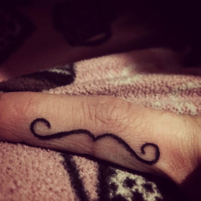 Finger tattoo with a simple black mustache design, commonly requested by tattoo enthusiasts.