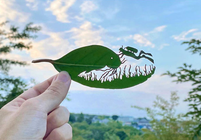 Hand holding a leaf vignette with intricate cutouts of a fish and insect created by a Japanese artist from leaves.