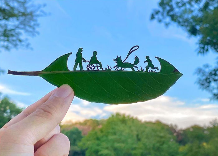 Hand holding a leaf with intricate cutouts of people and a dog, showcasing cute vignettes from leaves outdoors.
