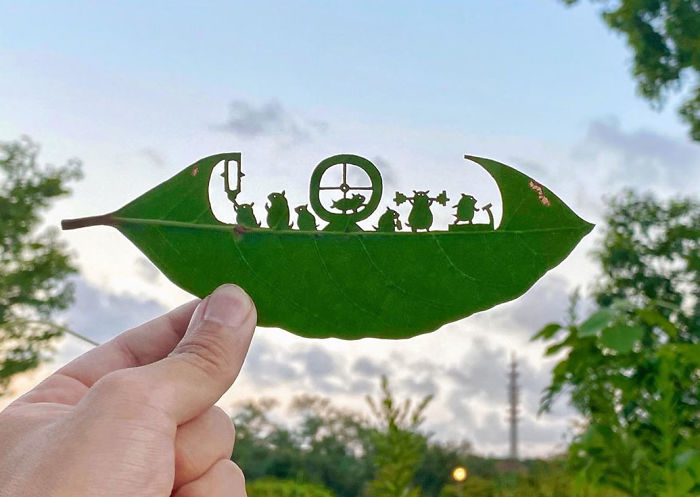 Hand holding a leaf with intricate cutouts forming a cute vignette scene by a Japanese artist.