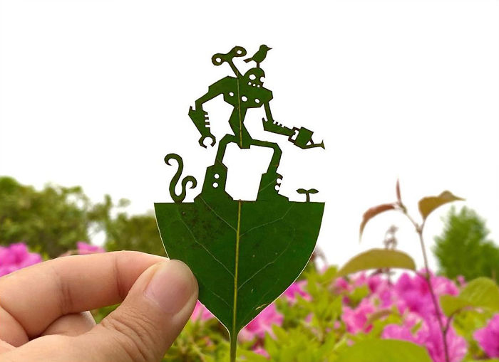 Hand holding a leaf with a delicate robot and bird vignette cutout showcasing Japanese artist leaf art.