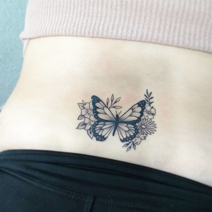 Butterfly tattoo with floral elements on lower back, a popular design often requested by tattoo enthusiasts.