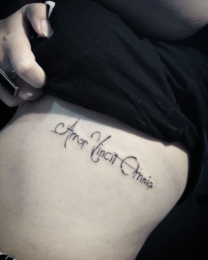 "Latin script tattoo design reading 'Amor Vincit Omnia' on a person's side."