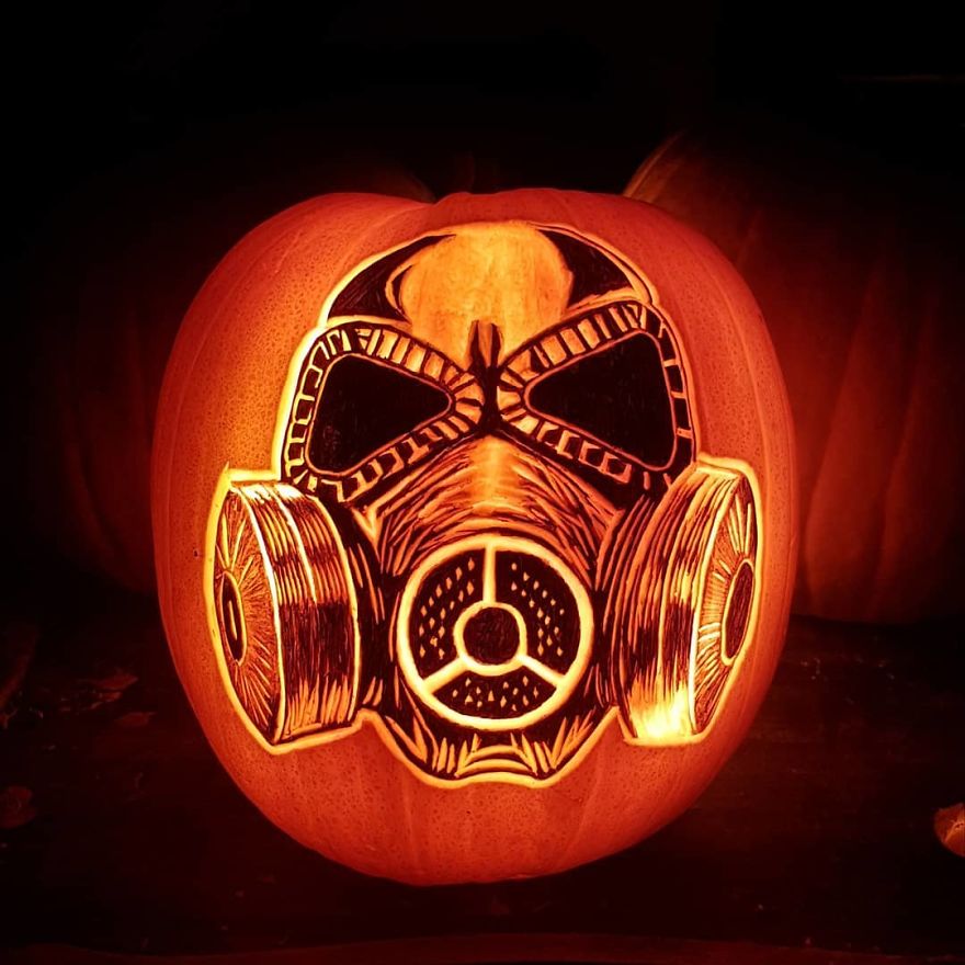 Pumpkin carving depicting a horror scene character wearing a gas mask, illuminated from within.