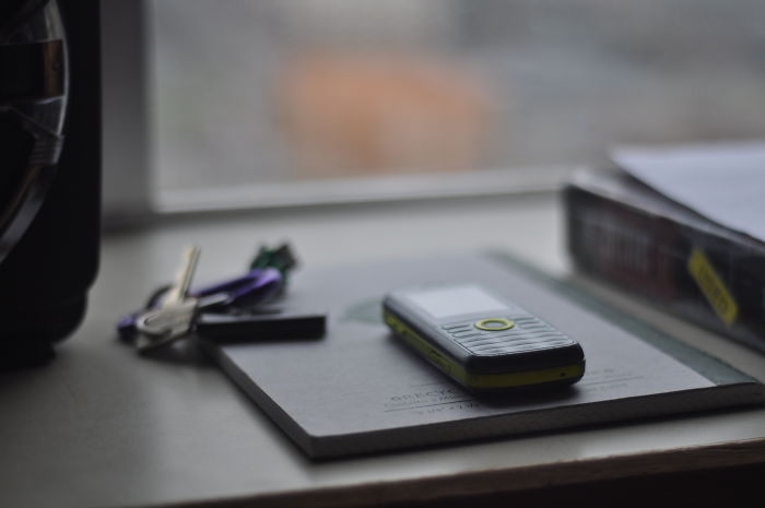 Old mobile phone lying on a notepad beside keys on a desk, illustrating funny moments of stupidity stories.