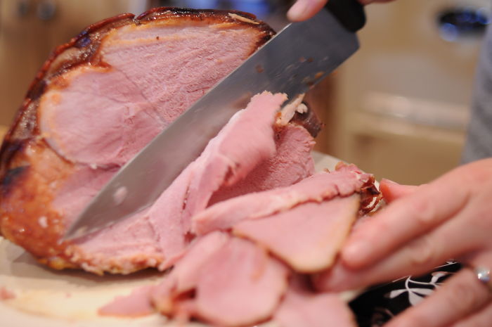 Person carving slices of ham on a wooden board, capturing a funny moment related to stupid stories on a new level.