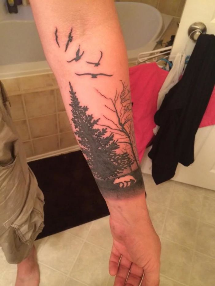 Forest and wildlife tattoo on forearm, featuring silhouetted trees and birds, represents overly requested tattoo designs.
