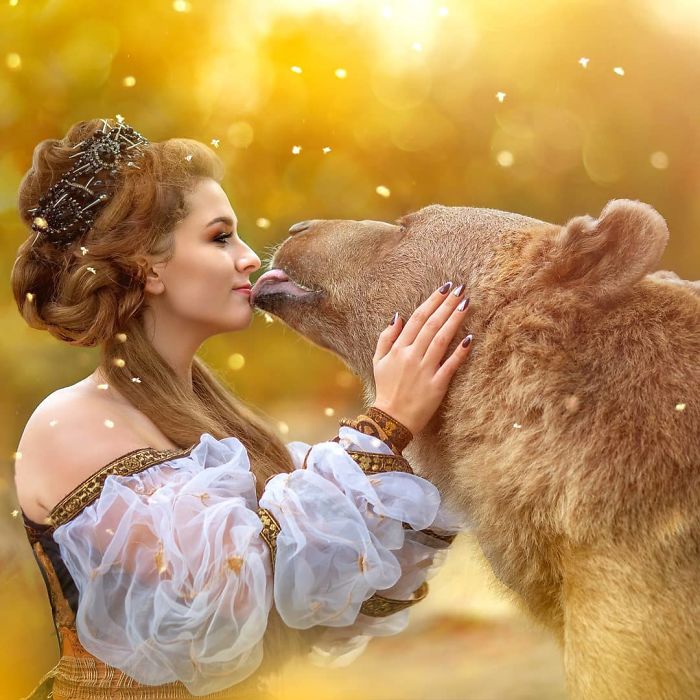 Woman in ornate dress gently touching a Russian brown bear cub, highlighting their close bond and modeling connection outdoors.