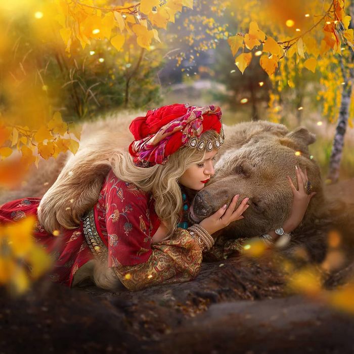 Woman in traditional attire gently cuddling a Russian brown bear in an autumn forest setting, showcasing bond and modeling.