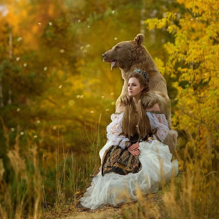 Russian brown bear posing with a woman in an elaborate dress outdoors during autumn, showcasing an unusual modeling scene.