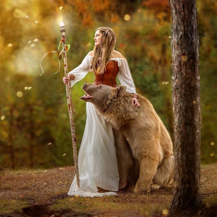 Woman in medieval dress with Russian brown bear in autumn forest, showcasing abandoned cub raised by humans modeling career.
