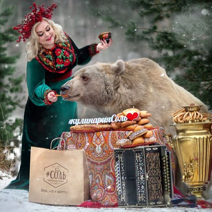 Russian brown bear feeding with a woman in traditional attire, surrounded by pastries and a samovar in a snowy forest.