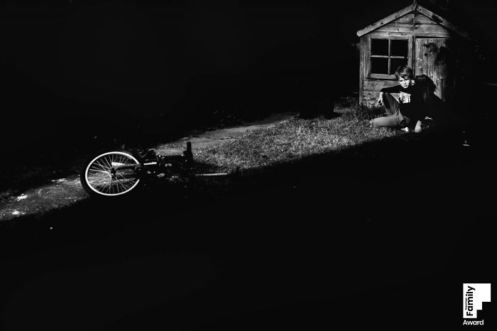 Black and white photo showing the art of capturing a family moment with a child near a small wooden shed and bicycle.
