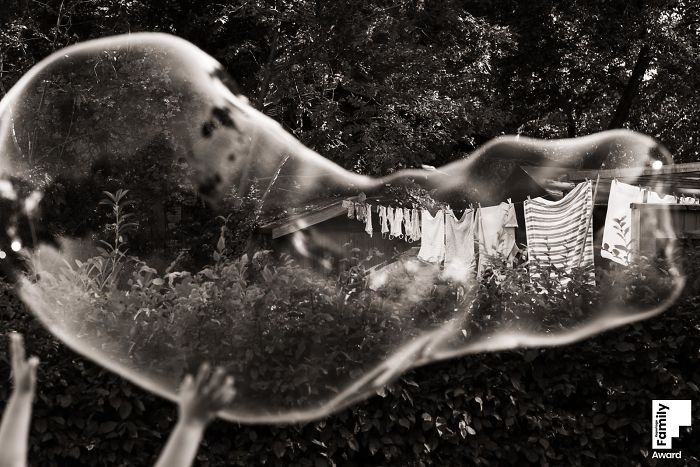 Large soap bubble floating outdoors with hands reaching up, showcasing the art of capturing a family moment in photography.