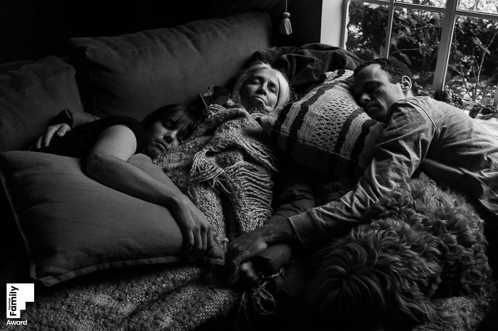 Black and white photo capturing a peaceful family moment with three generations resting closely on a couch with a dog nearby.
