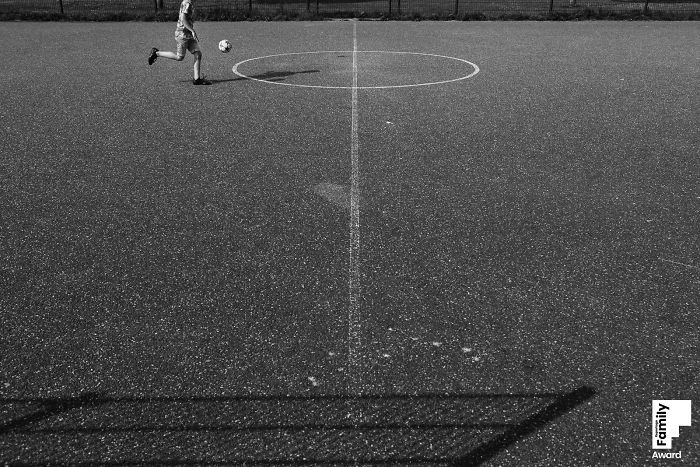 Child playing soccer alone on an empty field, capturing a family moment with artistic black and white photography.