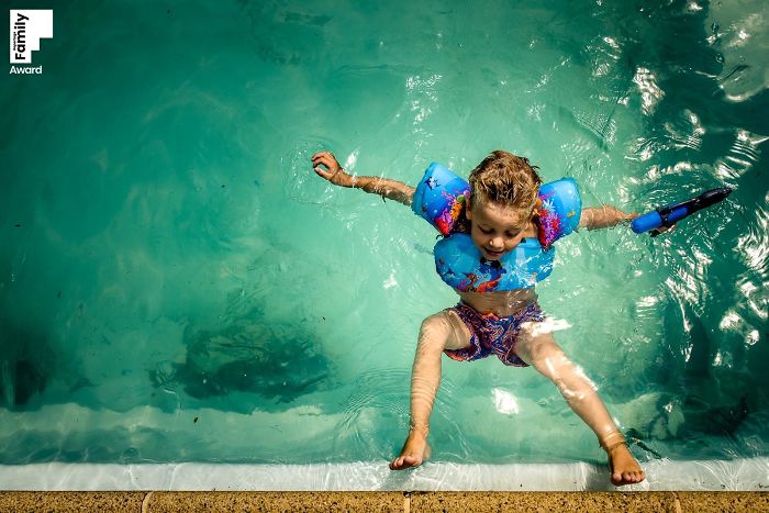 Child wearing floaties and playing in a pool, showcasing award-winning family moment photography capturing joyful outdoor fun.