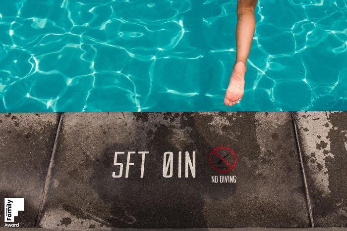 Child's leg dangling into a pool above 5ft 0in depth marking with a no diving sign, capturing a family moment.