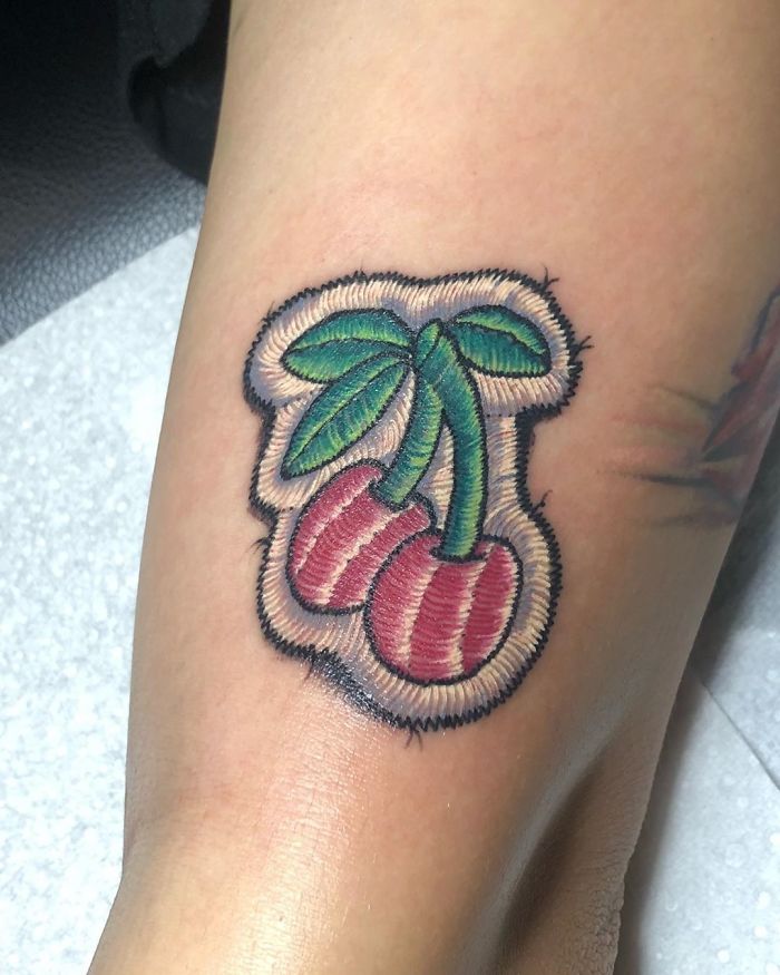 Tattoo resembling a sewn-on patch of cherries, showcasing intricate detail and vibrant colors.
