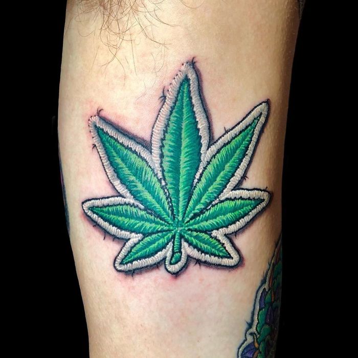 Tattoo resembling a sewn-on patch of a green leaf on skin, showcasing artistic tattoo creativity.