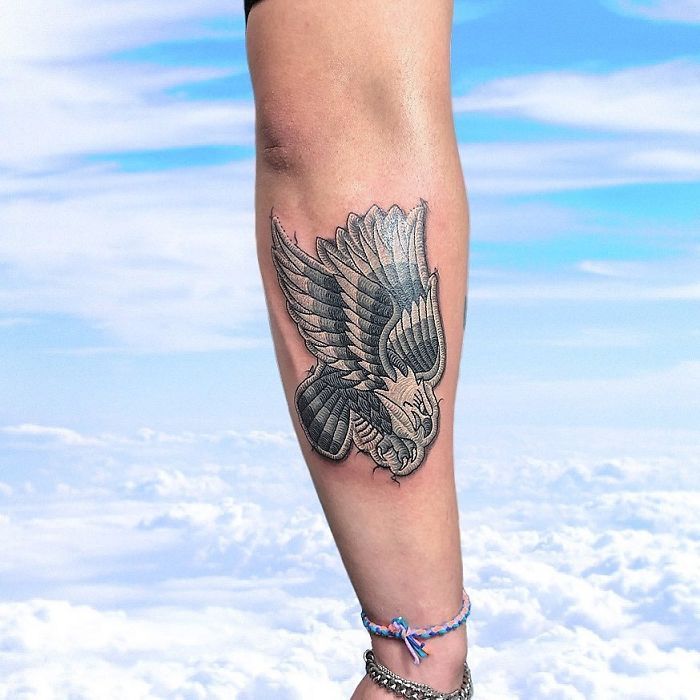 Tattoo resembling a sewn-on patch of an eagle on a person's leg against a clear sky background.