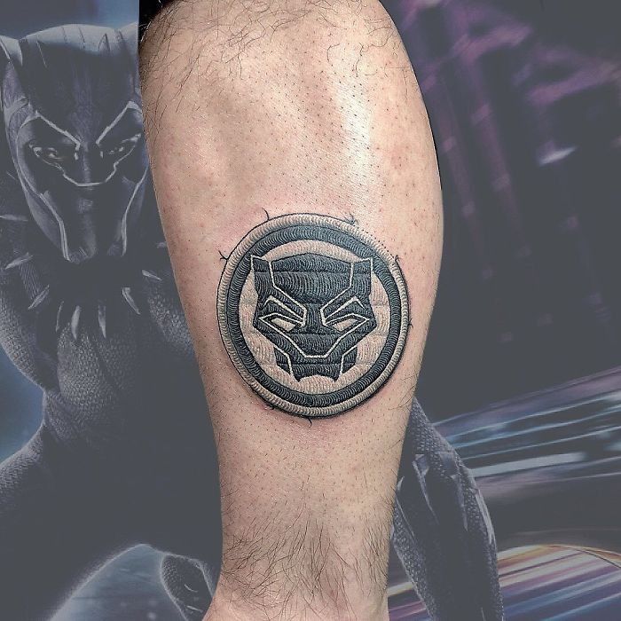 Tattoo resembling a sewn-on patch with a Black Panther design on a person's calf.