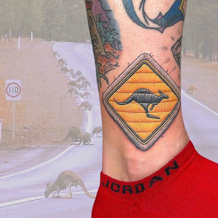 Tattoo resembling a sewn-on patch with a kangaroo sign on a person's leg wearing a red sock.