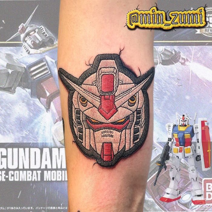 Tattoo of a Gundam robot head resembling a sewn-on patch on someone's arm.