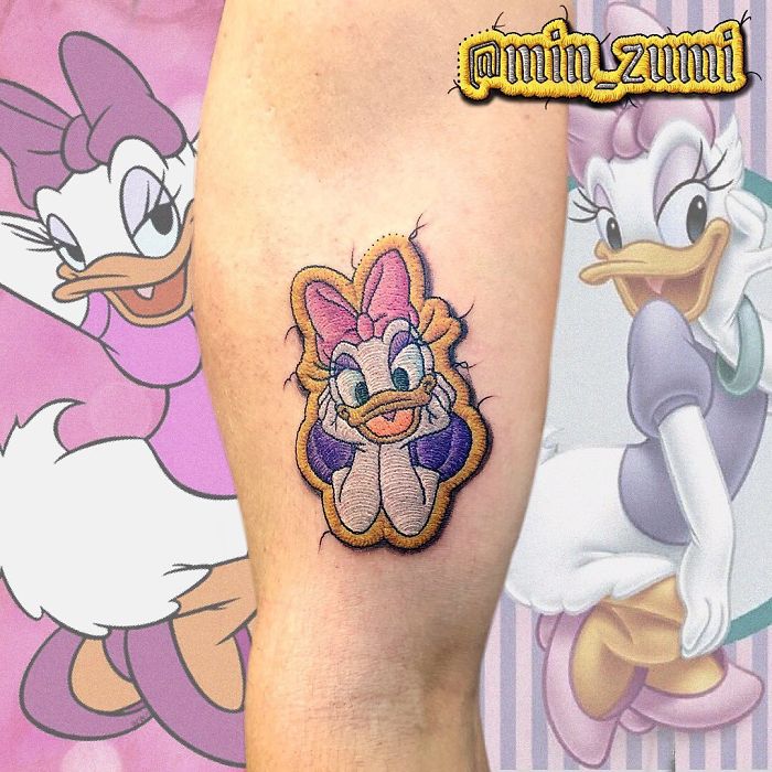 Tattoo resembling a sewn-on patch with a cartoon character design on a person's leg.