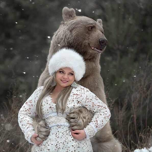 Russian brown bear posing with a woman in winter attire during a snowy outdoor photo shoot for modeling career.