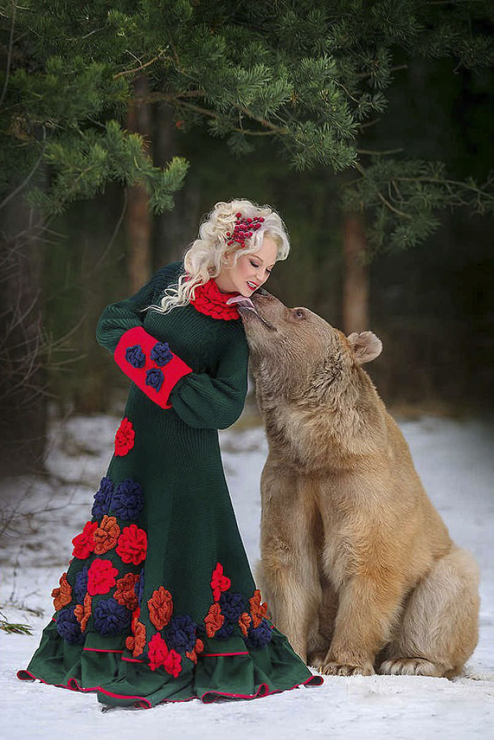 Woman in floral dress posing outdoors with a Russian brown bear who was raised by humans after abandonment.