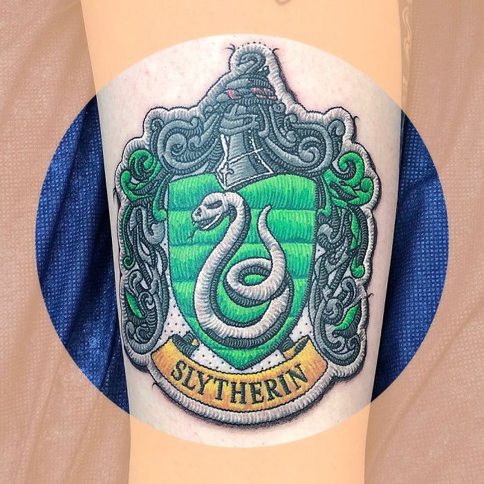 Tattoo resembling a sewn-on patch of a green and silver crest with a snake, labeled "Slytherin".