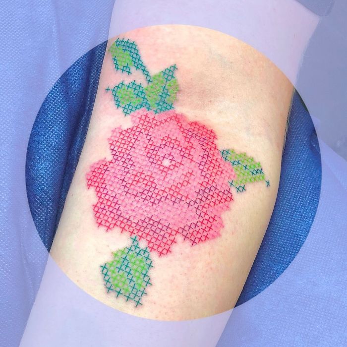 Tattoo resembling a sewn-on patch featuring a pink rose with green leaves on skin.