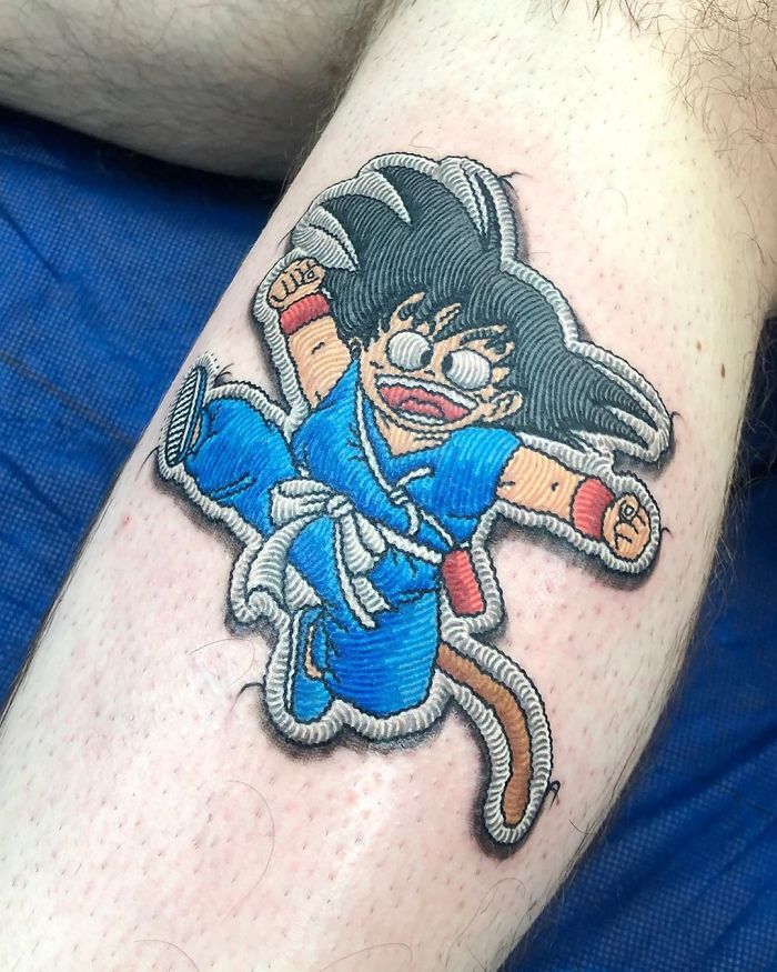 Tattoo of an animated character in blue outfit, designed to look like a sewn-on patch on skin.