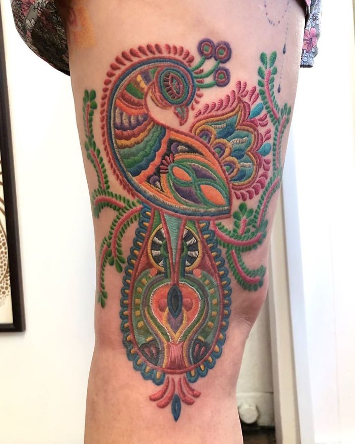 Colorful sewn-on patch style tattoo with intricate patterns and peacock design on leg.